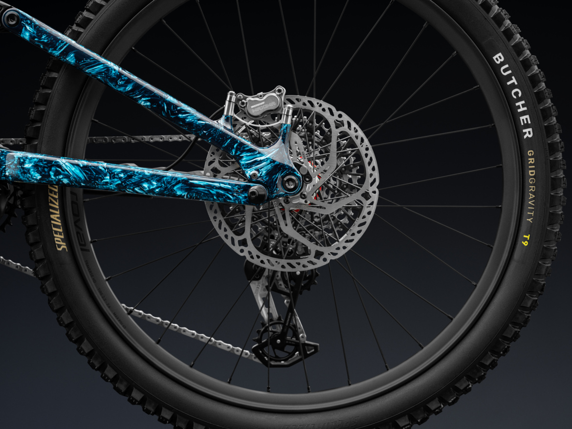 Close-up view of a mountain bike's rear wheel, showcasing the colorful blue and black frame, disc brake, and prominent tire labeled "Butcher Gridgravity T9." The image focuses on the intricate details of the bike components against a dark background.