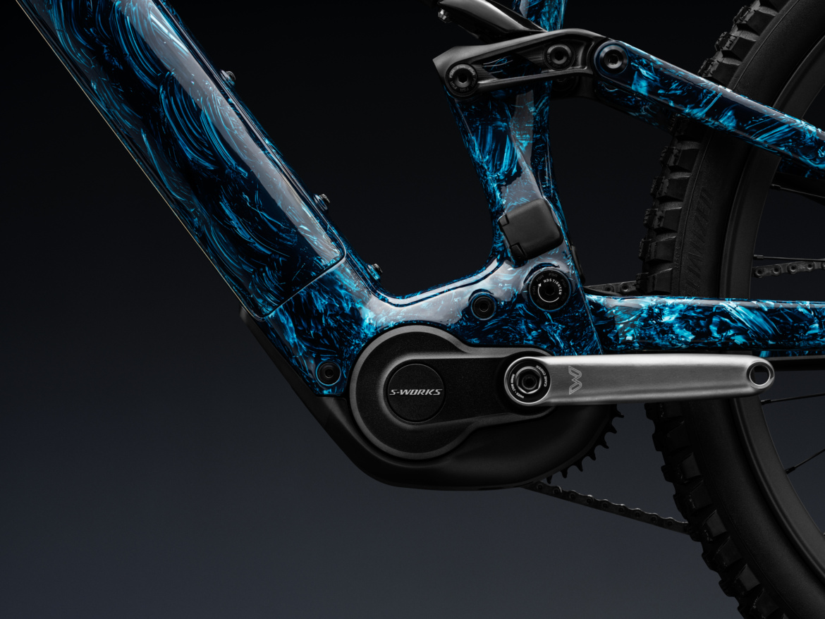 Close-up view of a mountain bike's frame featuring a striking blue and black swirl pattern, showcasing the motor and crankset. The image highlights the detailed design elements and components, set against a dark background for contrast.