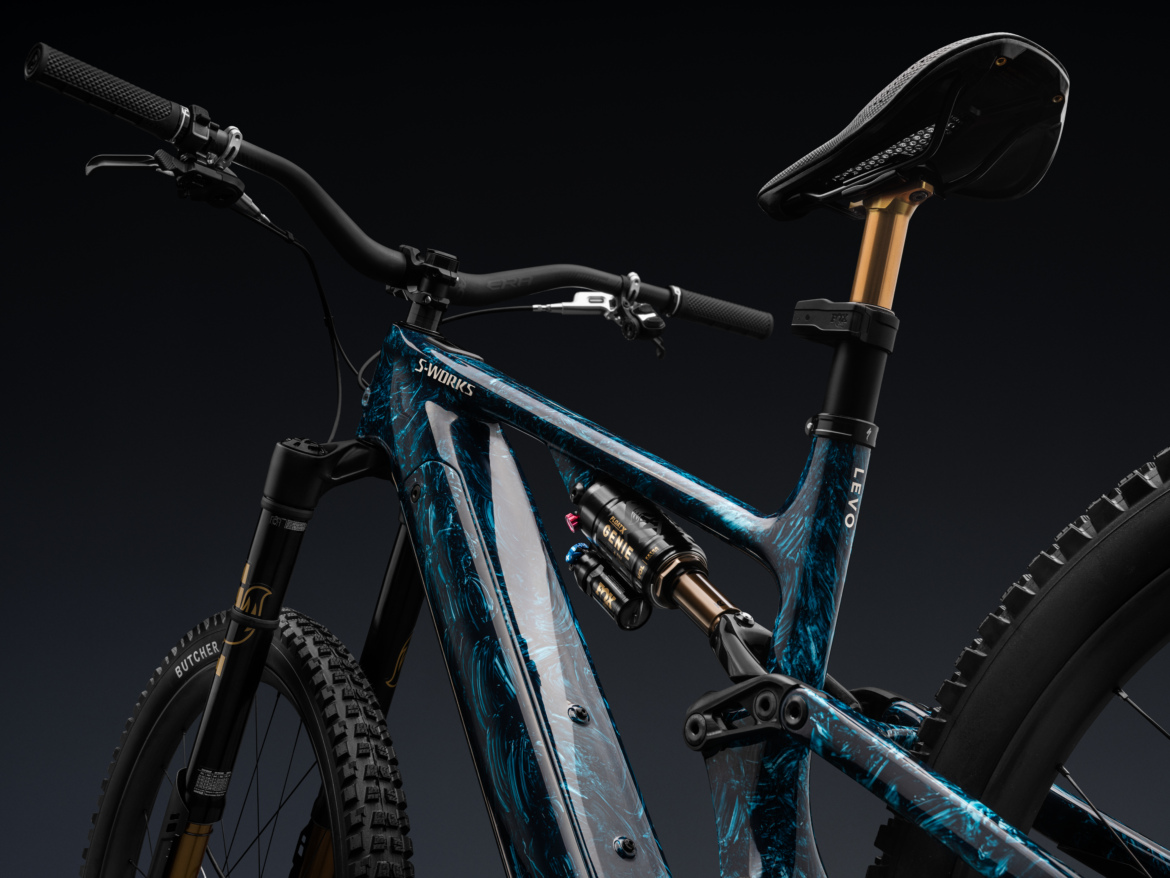 Close-up of a modern mountain bike featuring a blue and black marbled frame, high-performance suspension components, and a sleek design. The handlebars are equipped with grips, and the seat post has a gold finish, showcasing the bike's advanced engineering and aesthetic appeal.