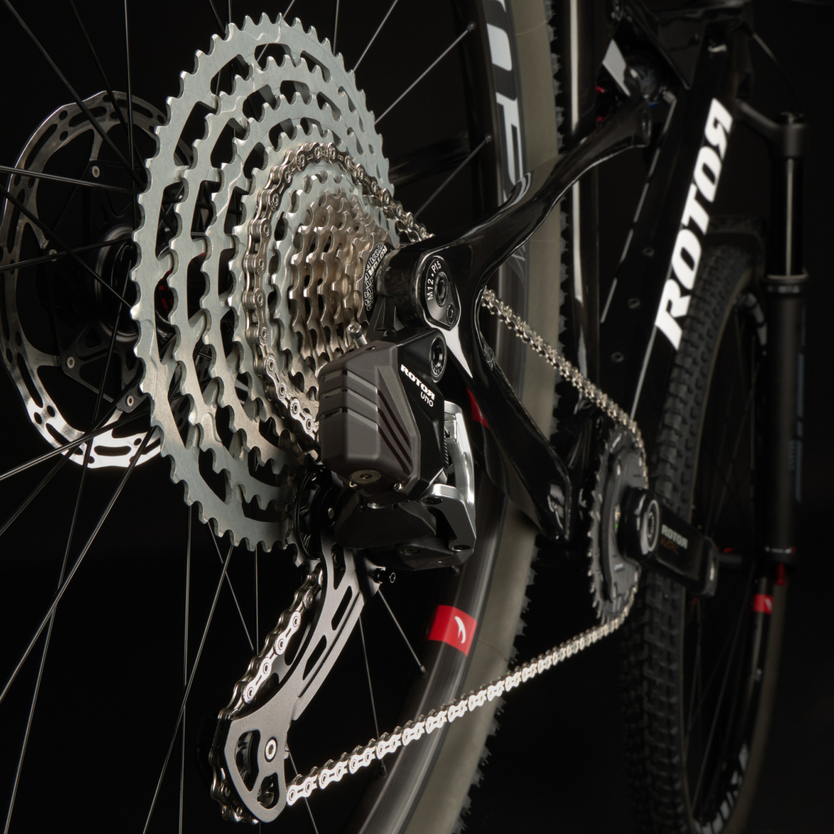 Close-up view of a bicycle's rear drivetrain, featuring a silver cassette, black derailleur, and chain, set against a dark background. The image highlights the intricate details of the components, showcasing their design and functionality.