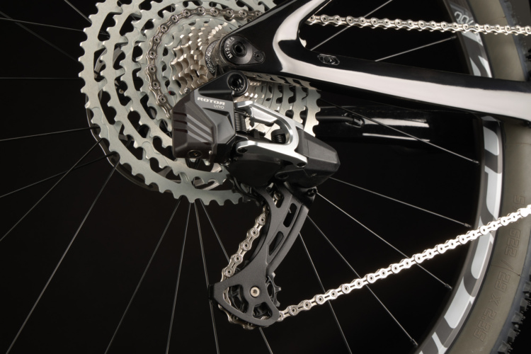 Alt text: Close-up view of a bicycle's rear derailleur and cassette, featuring a black and silver design, with a chain running through the derailleur and a dark background.