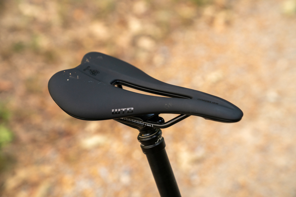 Black bicycle saddle mounted on a seat post, with a blurred natural background.