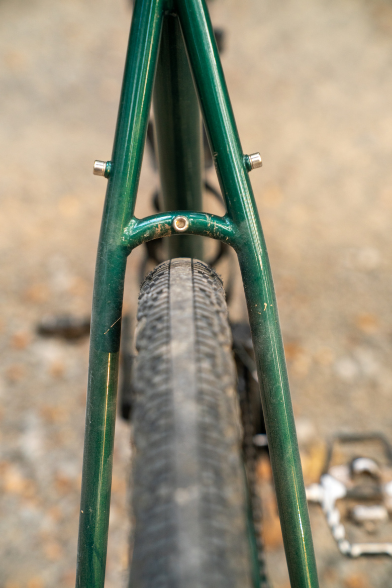 Close-up view of a green bicycle frame, focusing on the rear triangle and tire. The image highlights the structured metal frame and textured tire tread against a blurred background.