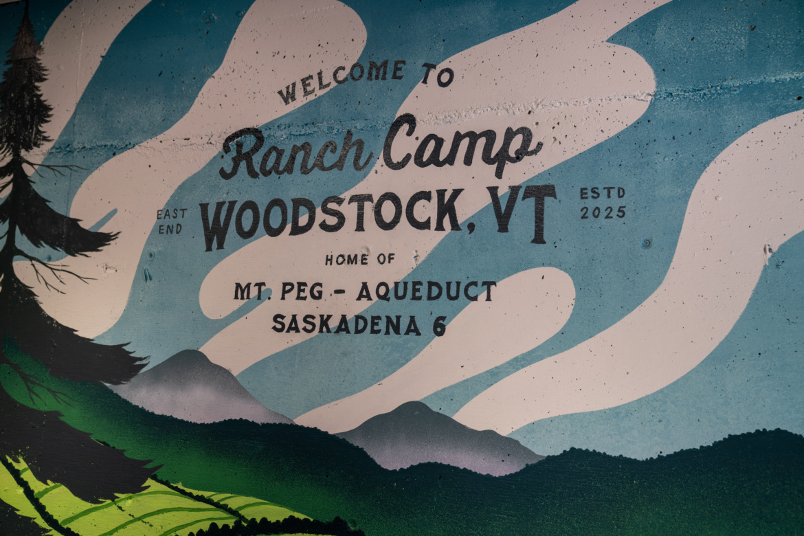 A colorful mural featuring welcoming text for "Ranch Camp, Woodstock, VT," with artistic representations of mountains, trees, and a blue sky. The mural includes the establishment year 2025 and highlights attractions like "Mt Peg - Aqueduct" and "Saskadena 6."