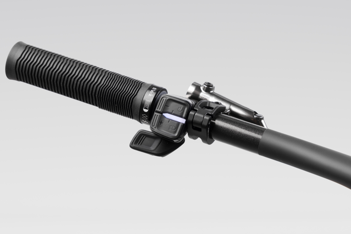 Close-up view of a bicycle handlebar grip featuring a textured surface for improved grip, along with a multi-function control switch mounted on the side. The design includes buttons for various functions and is attached to a sleek black bar, with a minimalistic background for focus.