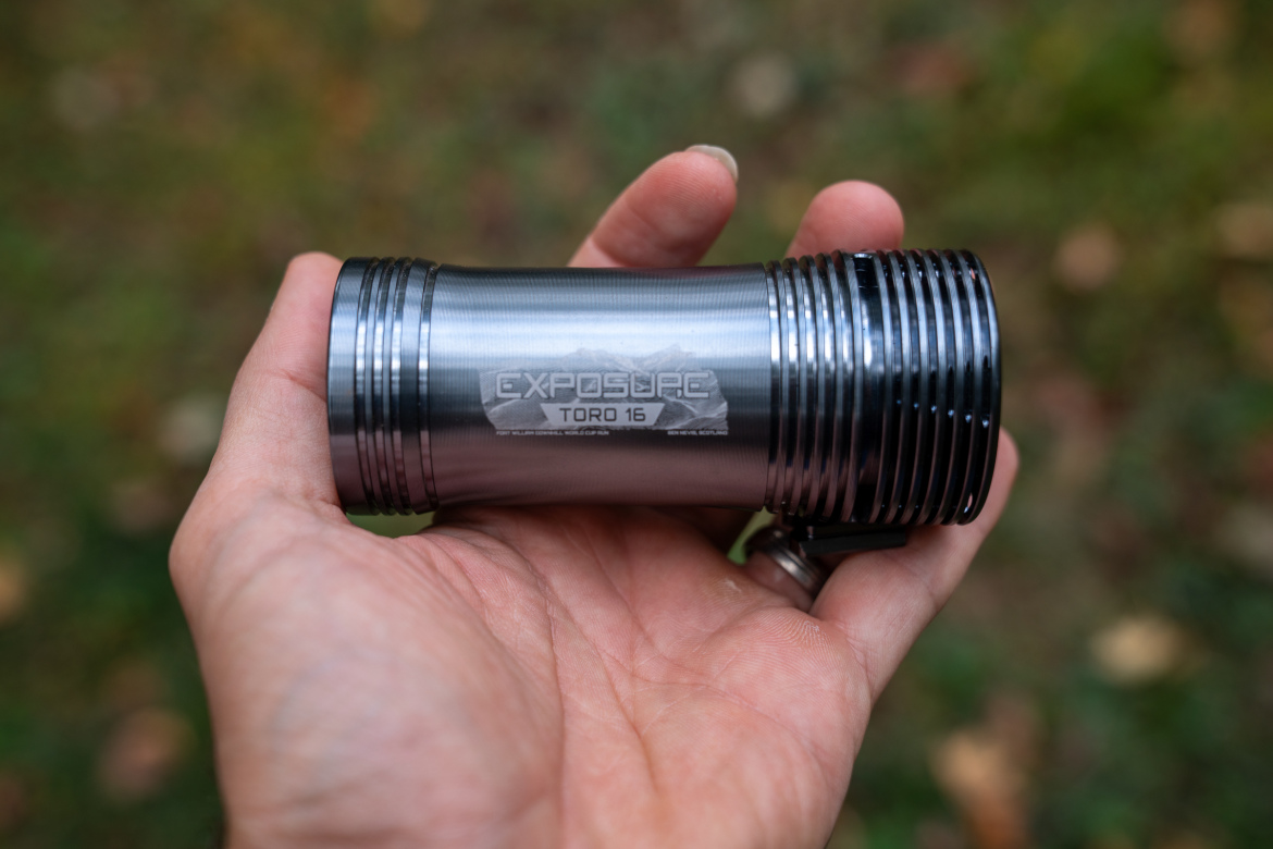 A person holding a Exposure Toro 16 bike light with a machined grip, set against a blurred natural background.