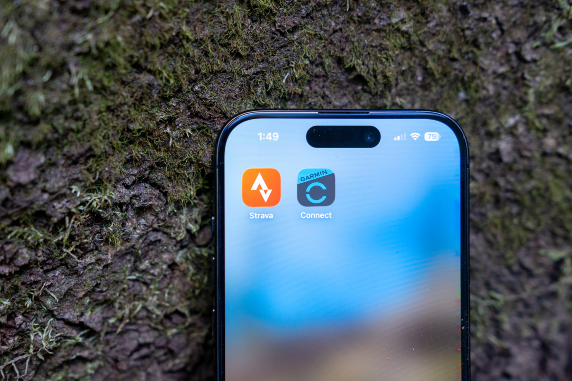 A smartphone screen displaying the Strava and Garmin Connect app icons, set against a textured natural background that resembles tree bark. The time on the phone shows 1:49, and the battery indicator is at 79%.