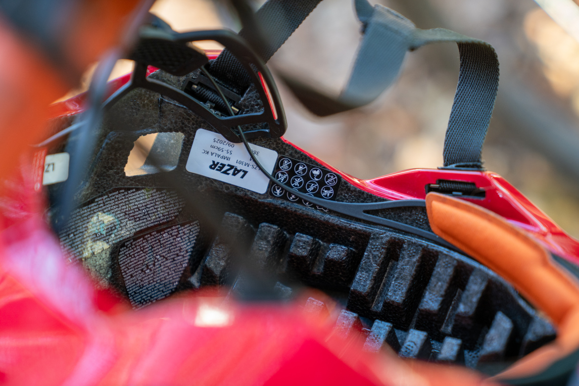 Close-up of the interior of a red cycling helmet showing padding, adjustable straps, and safety labels.