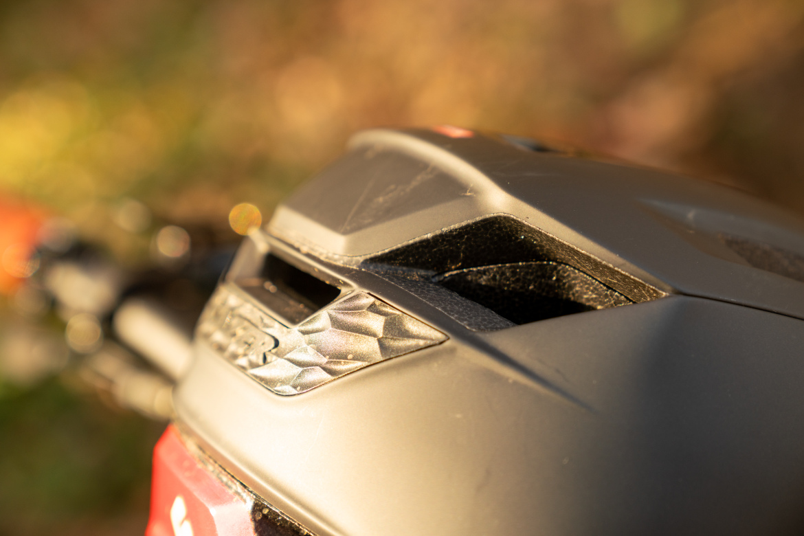 Close-up of a black helmet with ventilation openings, showcasing intricate details and textures against a blurred natural background.