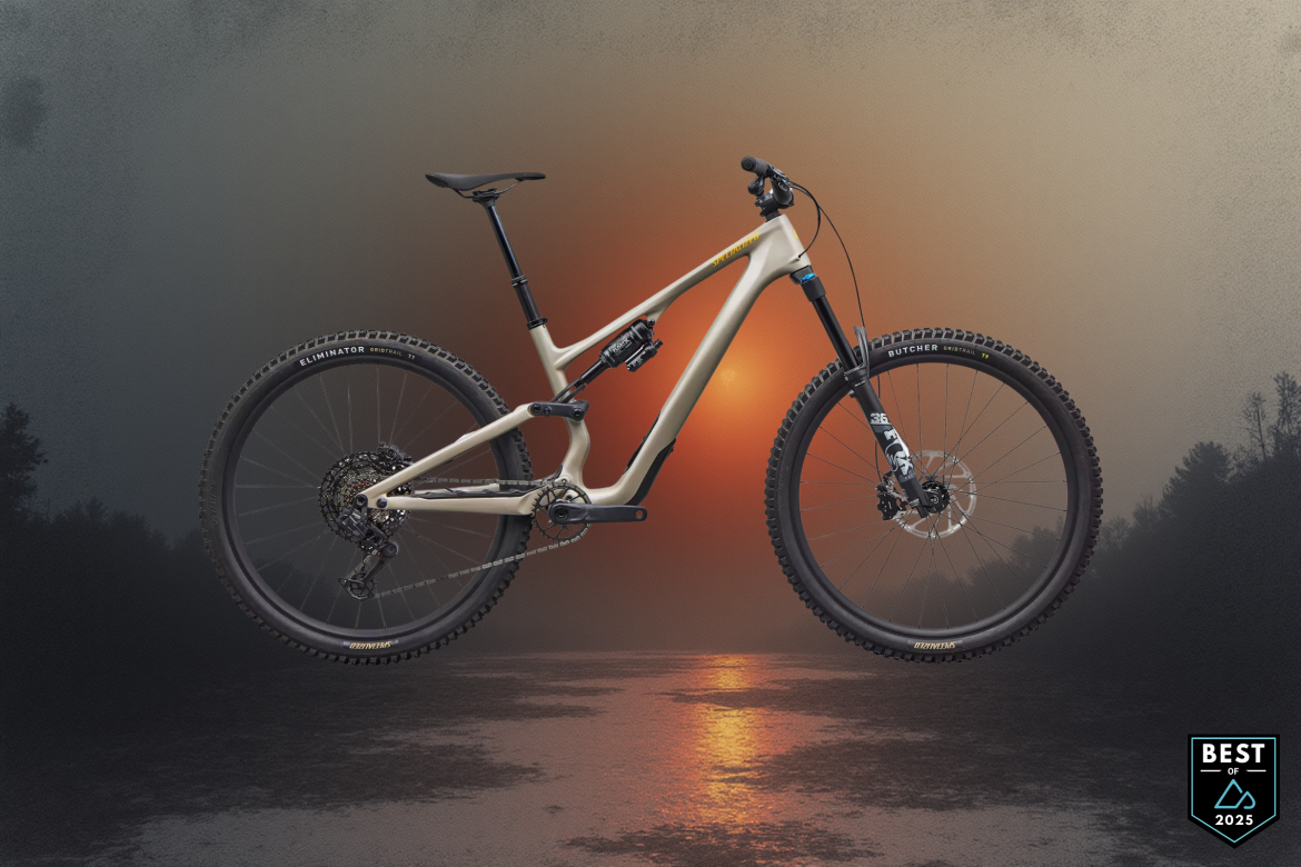 A modern mountain bike suspended in mid-air against a scenic, foggy background featuring a sunset over water. The bike is a light tan color with high-quality components, including wide tires labeled "Eliminator" and "Butcher." A badge in the corner indicates "Best of 2025."