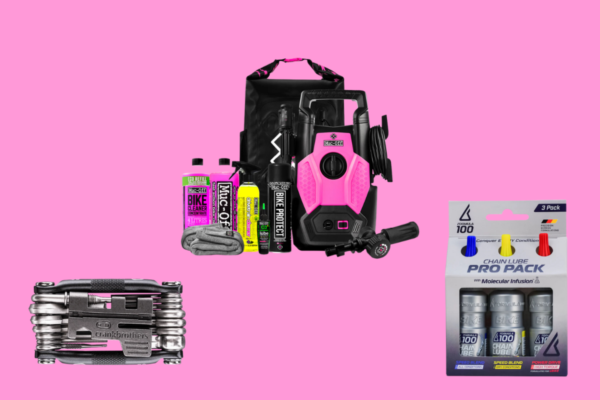 A collection of bicycle maintenance products displayed on a pink background. Items include a pink pressure washer, Muc-Off bike cleaner concentrate, Muc-Off bike protect spray, a microfiber cloth, a multitool from Crankbrothers, and a chain lube pro pack with three different types of chain lubricant.