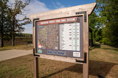 Sign displaying the map and trail system for Craighead Forest Park, including trail names, difficulty levels, and a note to "Ride The Ridge!" The sign is situated outdoors with trees and a grassy area in the background. Craighead Forest Park mountain bike trail.