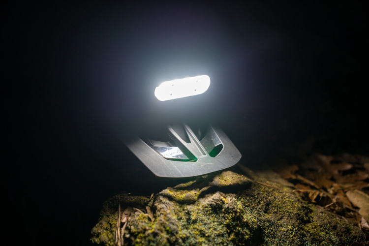 A bright LED light illuminating a rocky surface in a dark environment, with soft shadows and surrounding foliage.
