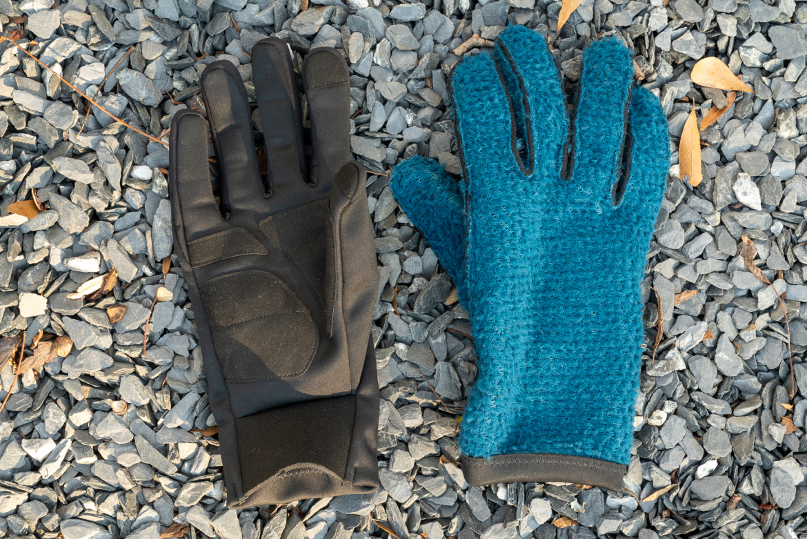 A black glove and a blue textured glove placed on a bed of gray gravel stones.