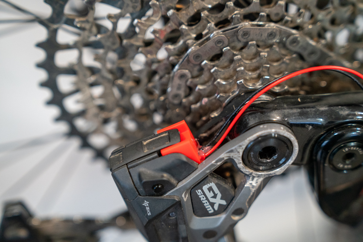 Close-up view of a SRAM GX derailleur with a visible red adjustment tab, mounted on a bicycle's cassette. The image showcases the intricate details of the chain mechanism and gears.