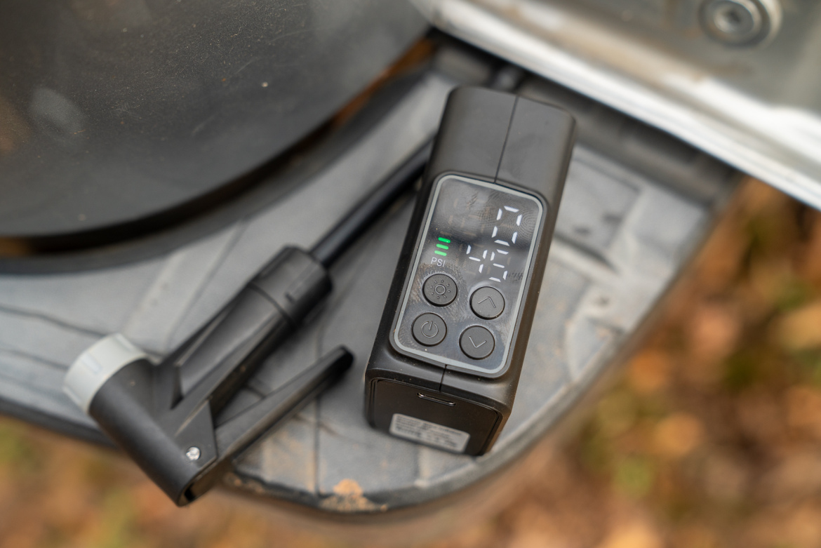 A digital air pressure gauge placed on a textured surface, displaying pressure readings and controls. A hose attachment is connected to the gauge, with a muted background that suggests an outdoor setting.