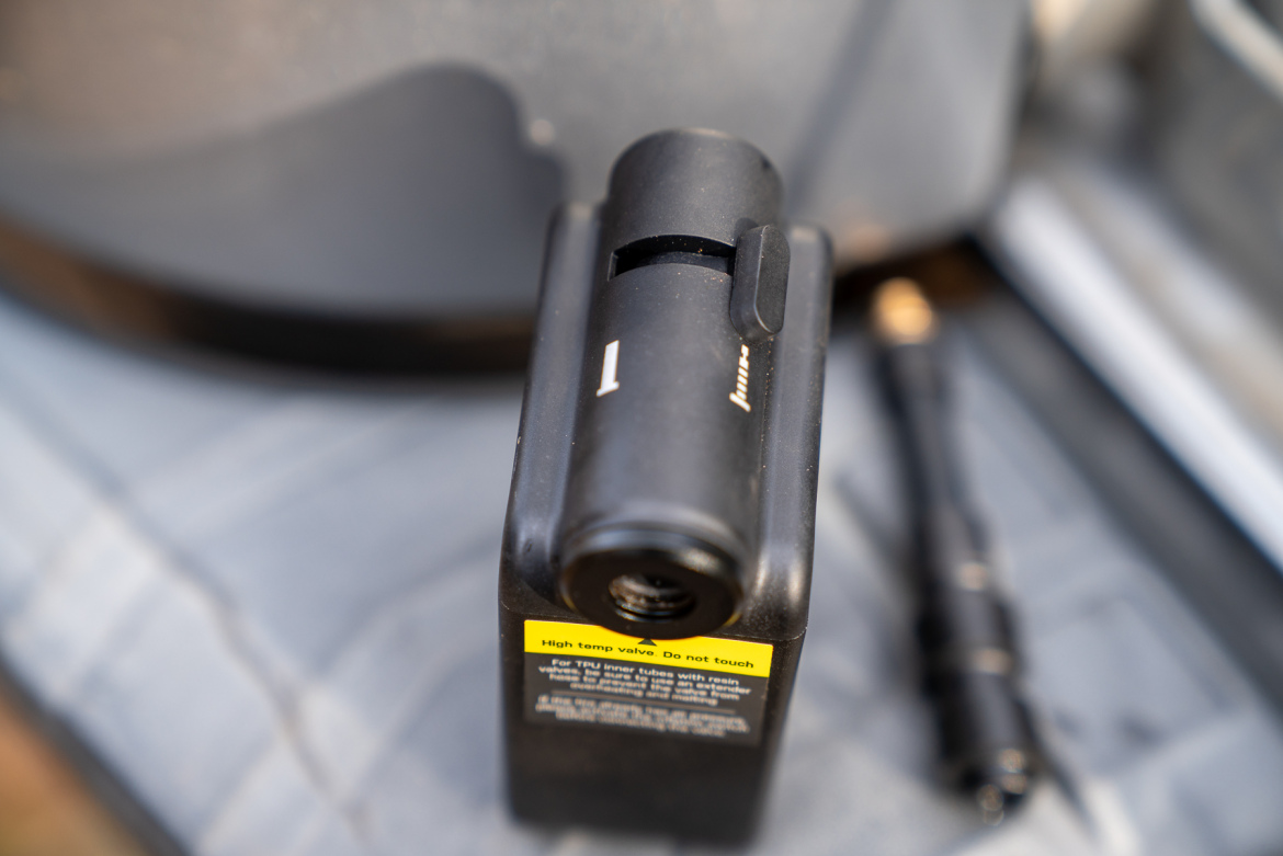 Close-up of a black device with a switch and a valve, featuring a warning label that reads "High temp valve. Do not touch." The device is resting on a gray surface, with another object partially visible in the background.