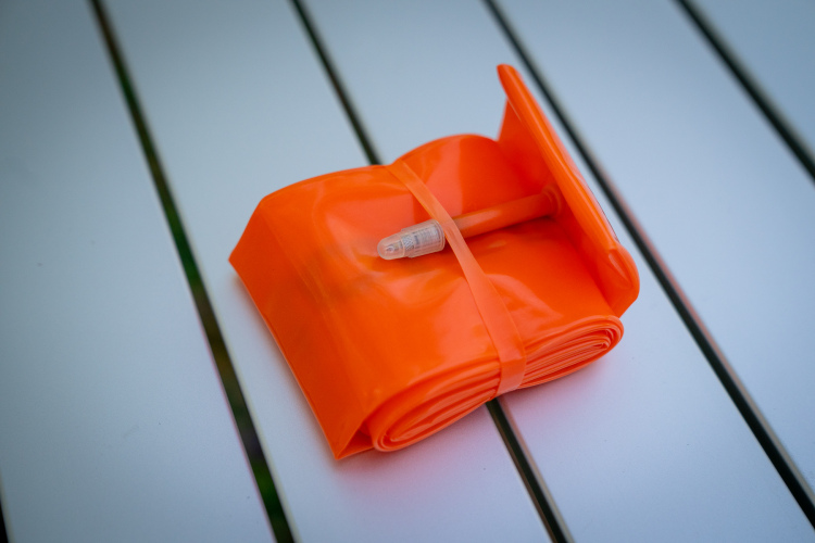 A rolled-up orange flexible strip with a small connector, resting on a white surface with parallel lines. The strip is secured with a band, and it appears to be made of a glossy material.
