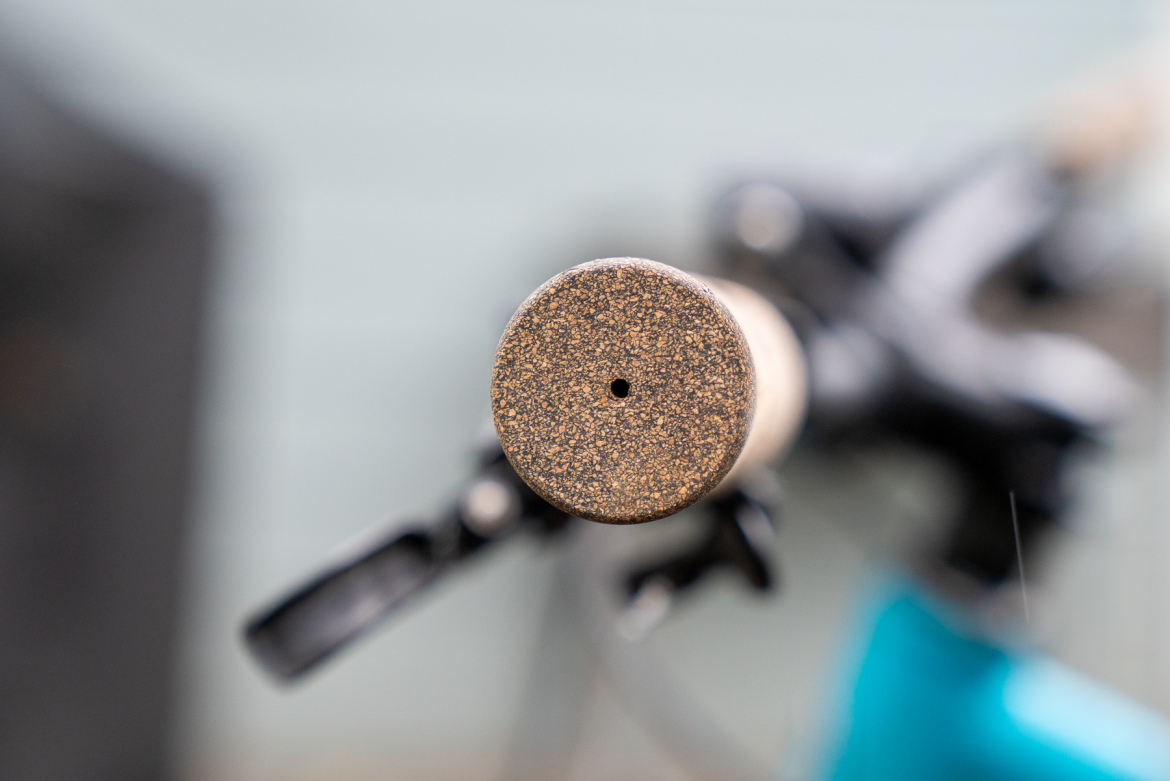Close-up view of the textured handle end of a fishing rod, featuring a small hole in the center. The background is blurred, highlighting the rod's grip and reel.