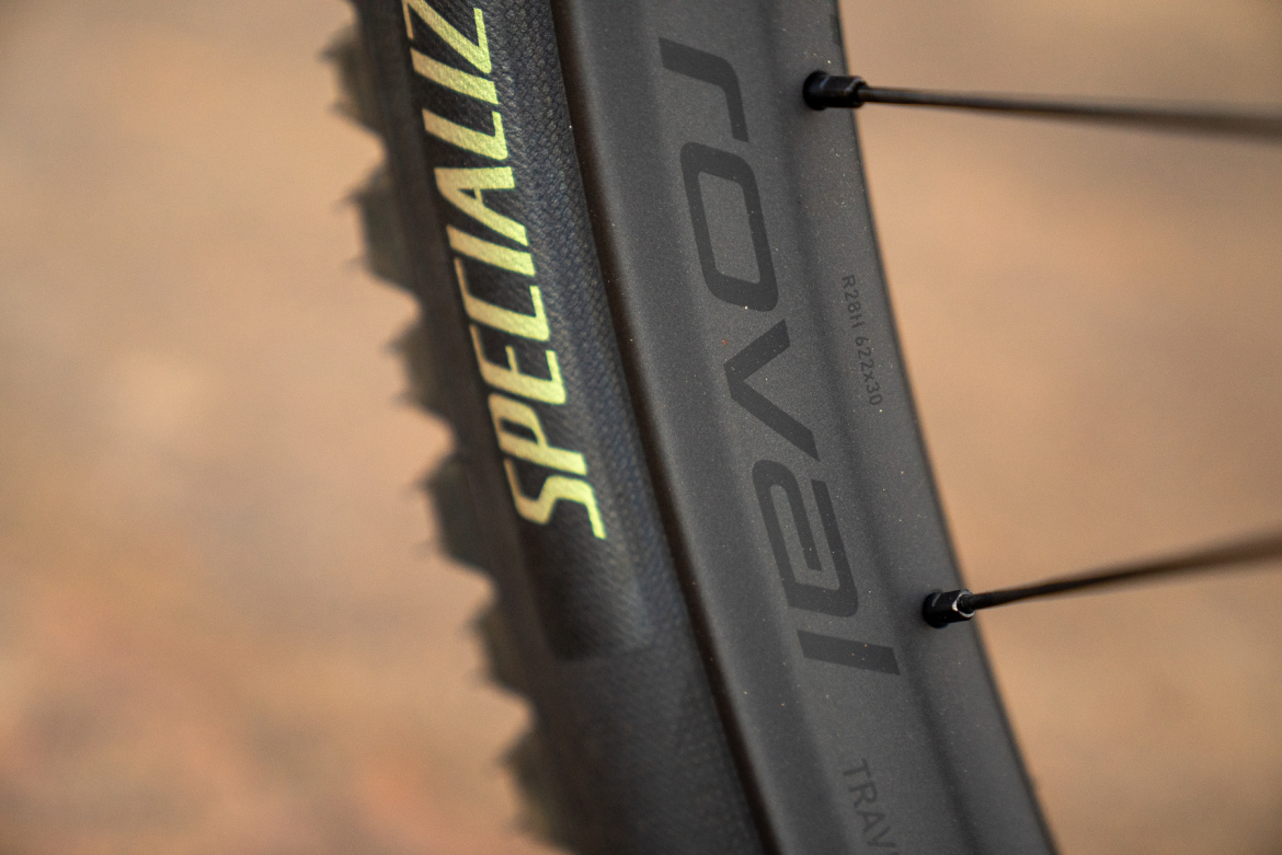 Close-up view of a black bicycle wheel, featuring the words "Specialized" and "Roval" on the rim. The image shows details of the tire and spoke, with a textured surface.