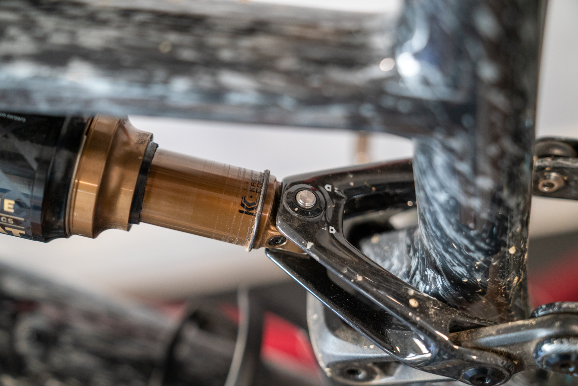 Close-up view of a bicycle's rear shock absorber mounted on the frame, showcasing the intricate details of the suspension system, including the adjustment settings and the carbon fiber texture of the bike frame.