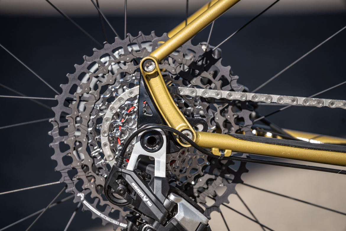 Close-up image of a bicycle's rear derailleur and cassette, showcasing a gold and black color scheme, with a focus on the gears and chain. The components are designed for precision shifts in a high-performance bicycle setup.