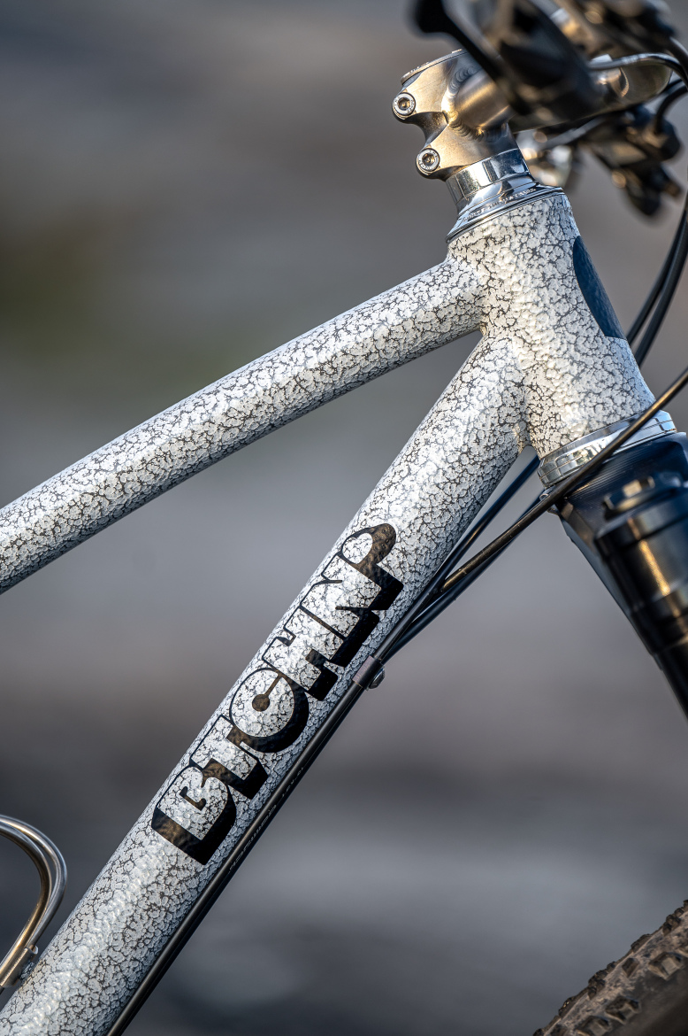 Close-up view of a bicycle frame featuring a textured, crackle finish in gray and white, with the brand name "BITCHAP" prominently displayed in bold black letters. The image captures the details of the frame's design and components, emphasizing its rugged and unique appearance.