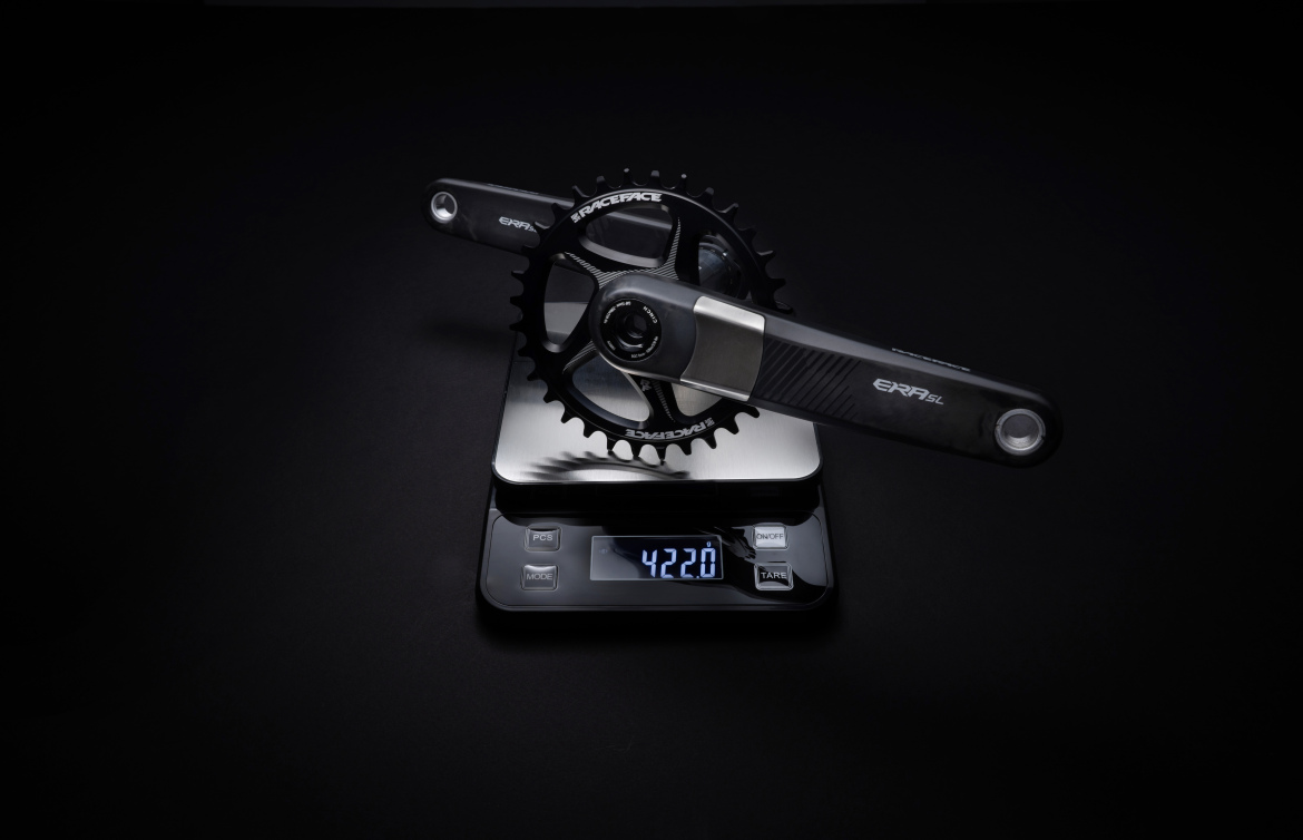 A black bicycle crankset with a chainring is placed on a digital scale, displaying a weight of 422 grams. The scale is on a dark surface, and the overall lighting emphasizes the sleek design of the crankset and its components.