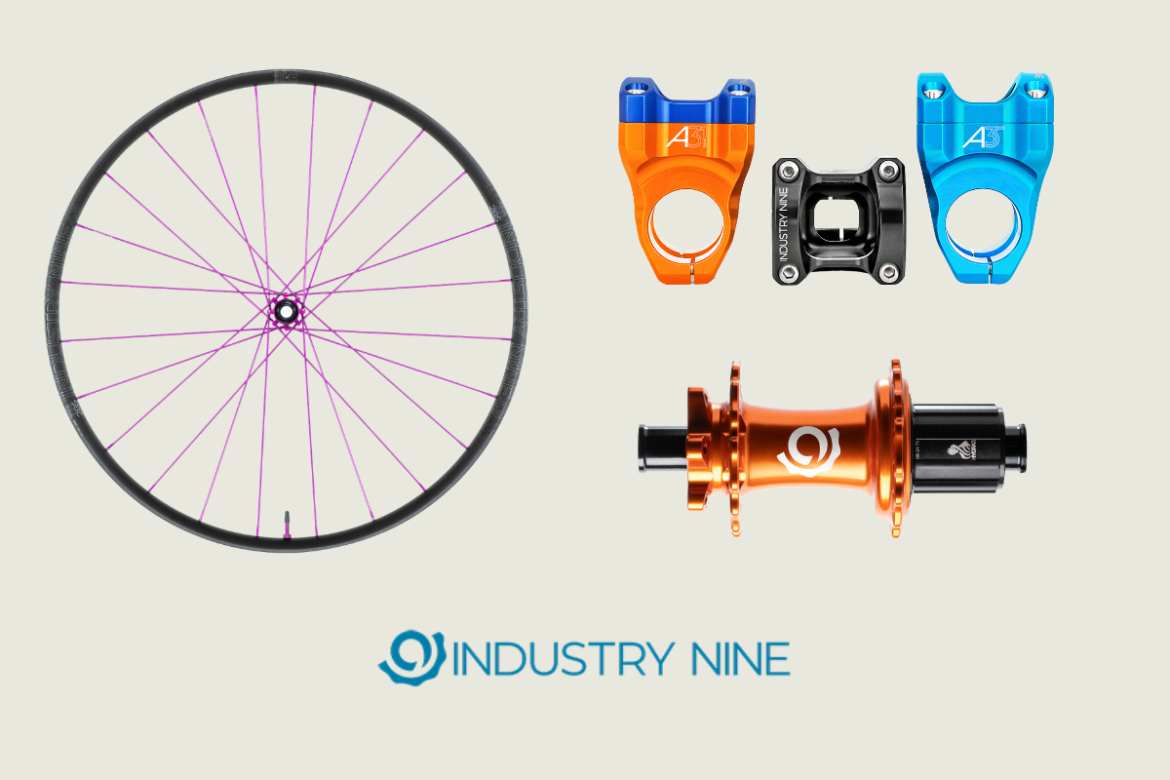 A bicycle wheel with purple spokes is displayed alongside various bicycle components, including two colored top caps (one blue, one orange), a black spacer, and an orange hub. The image features the Industry Nine logo at the bottom.