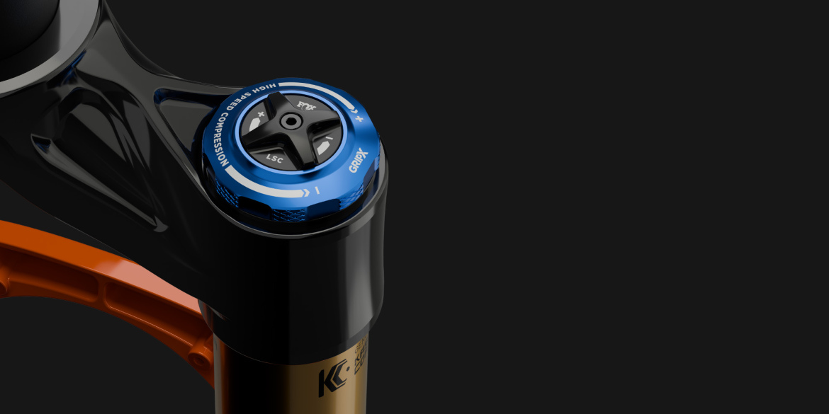 Close-up view of a black and orange bike suspension fork with a blue adjustment knob at the top, featuring markings for compression settings and high-speed adjustments, set against a dark background.