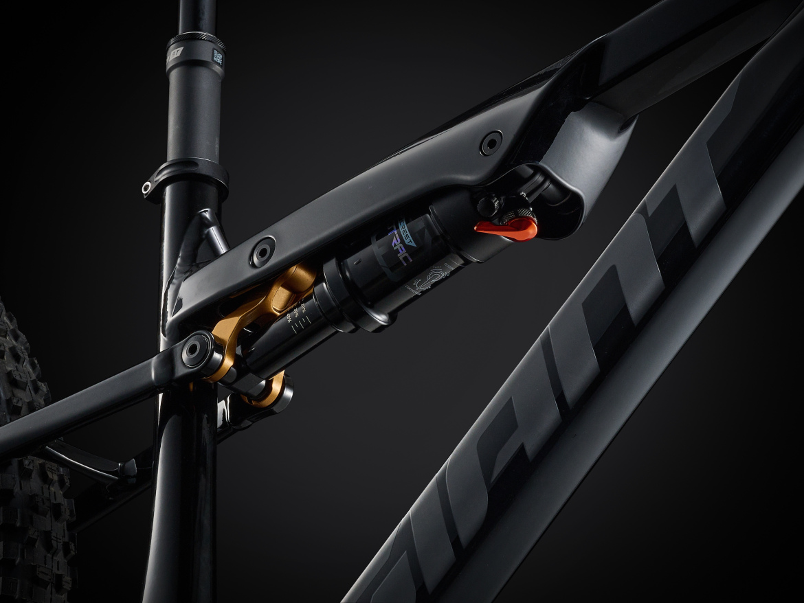 Close-up view of a mountain bike's suspension system, showcasing the shock absorber and linkage mechanism. The components feature a sleek black finish with gold accents, set against a dark background to emphasize the intricate details of the design.
