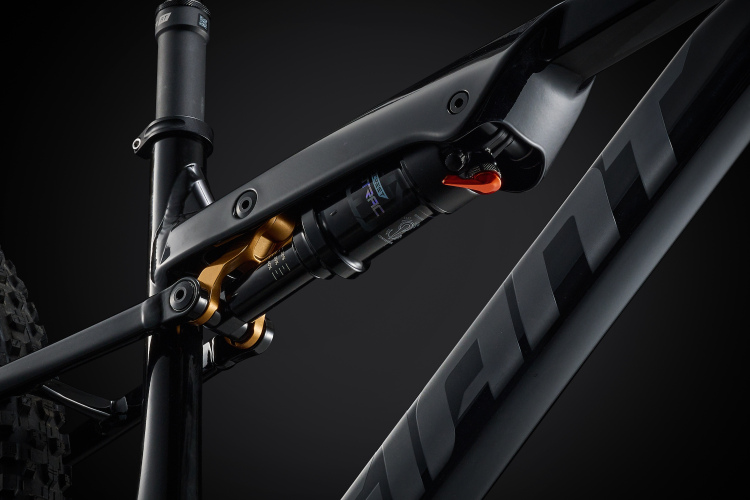 Close-up view of a mountain bike's suspension system, showcasing the shock absorber and linkage mechanism. The components feature a sleek black finish with gold accents, set against a dark background to emphasize the intricate details of the design.