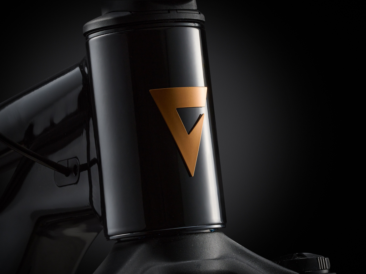 Close-up of a sleek black bicycle frame featuring a prominent copper-colored logo. The image highlights the smooth finish and modern design elements of the bike, set against a dark background.