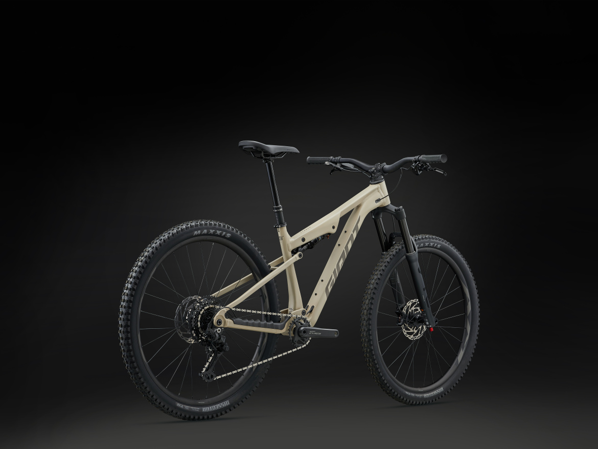 A modern mountain bike with a sleek, light beige frame, equipped with thick tires suitable for off-road terrain. The bike features a front suspension fork, a rear derailleur, and a stylish design, presented against a dark background for emphasis.