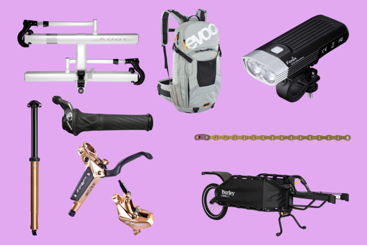 A collection of biking accessories displayed on a purple background, including a bike rack, a gray backpack, a bike light, a dropper seat post, a handlebar grip, two brake components, a bike chain, and a bicycle cargo trailer.