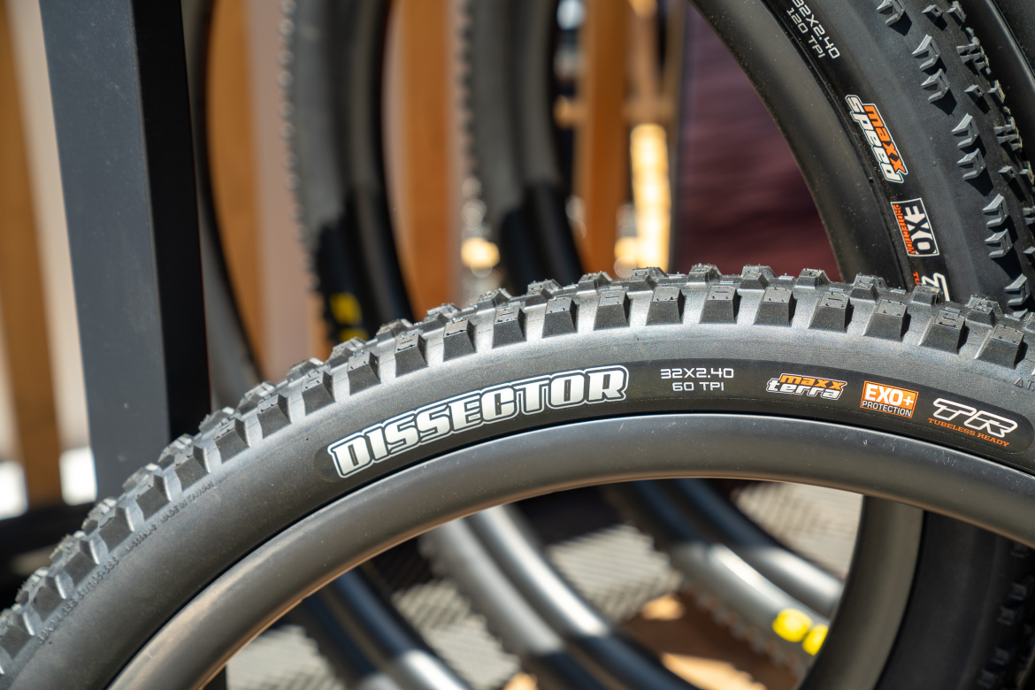 Close-up of a mountain bike tire labeled "DISSECTOR," measuring 32x2.40 with 60 TPI, featuring Maxx Terra compound and EXO+ protection. The tire is displayed among other bike tires in a retail setting.