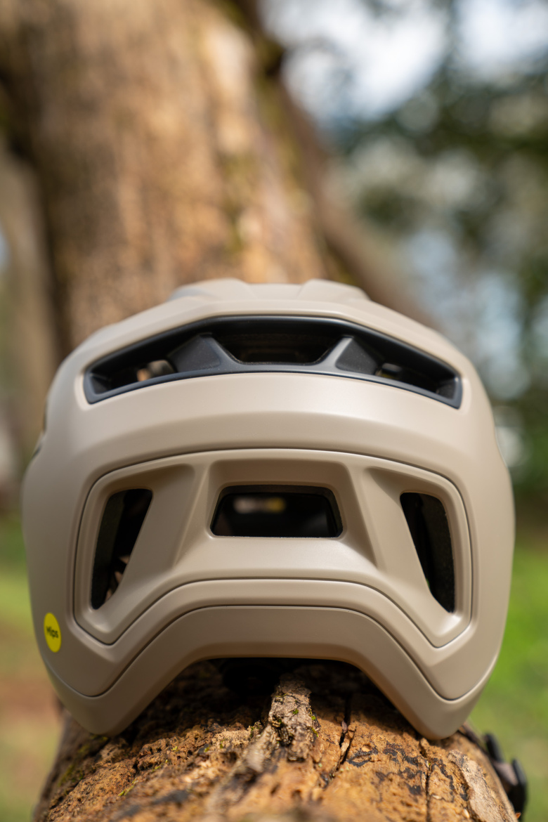 A beige bike helmet resting on a wooden log, with a blurred natural background. The helmet features vents and an adjustable fit system, emphasizing its design for safety and comfort during cycling activities.