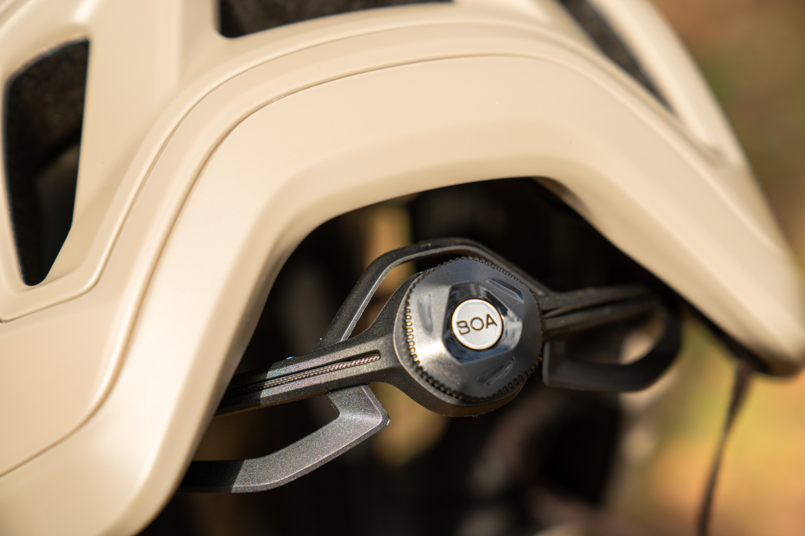 Close-up of a bike helmet's adjustable fitting system featuring a dial mechanism with the logo "BOA," set against a blurred background.