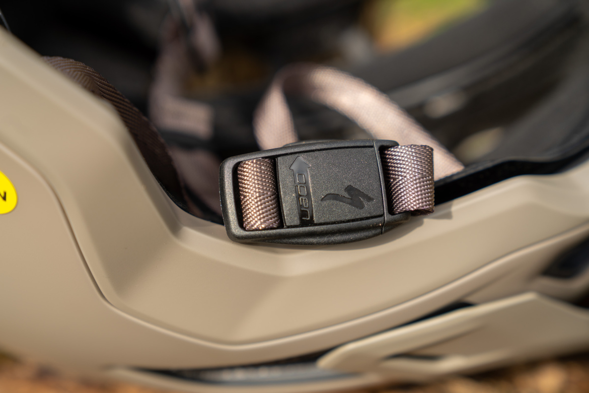 Close-up image of a tan bicycle helmet featuring a black buckle and adjustable straps, highlighting the safety features and design details.