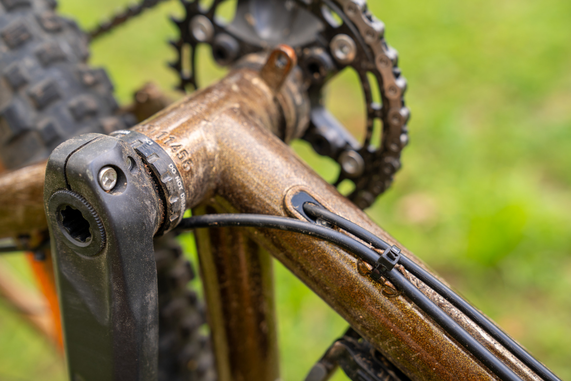 Close-up view of a mountain bike's crank and drivetrain, showcasing the intricate details of the bike's frame, chainring, and gear mechanism, with signs of dirt and use evident on the components.
