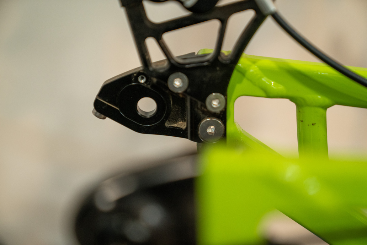 Close-up view of a bicycle frame, highlighting the connection between a black metal component and a bright green section of the frame. The image shows bolts and openings that are part of the bike's structural design. A blurred background adds depth to the focus on the frame details.