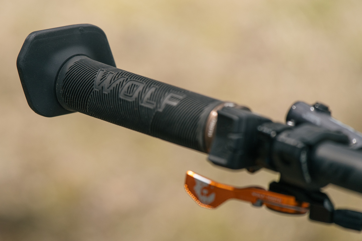 Close-up of a textured motorcycle grip featuring the word "WOLF," with a portion of the handlebar and an orange throttle adjustment lever in the background.