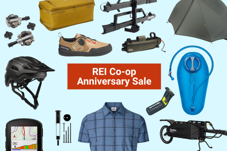 A collection of outdoor gear and apparel displayed on a light blue background, featuring a bike helmet, hiking shoes, a camping tent, a hydration reservoir, and various tools. The center includes a bold graphic announcing the "REI Co-op Anniversary Sale."