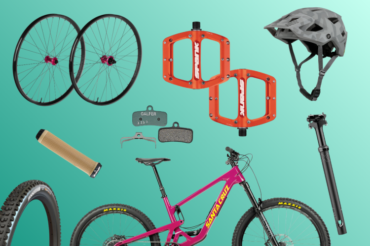 A collection of mountain biking components including two black and pink wheels, orange bike pedals, a grey helmet, brake pads, a bicycle seat post, a grip, and a pink mountain bike frame, all arranged on a teal background.