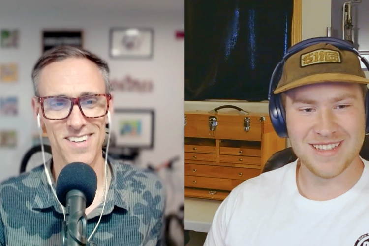 A split-screen video call featuring two men smiling at each other. The man on the left is wearing glasses and a patterned shirt, speaking into a microphone, with a blurred background showcasing framed artwork and bicycles. The man on the right is wearing a baseball cap and headphones, with a light-colored shirt, sitting in front of a wooden storage box and a dark background.