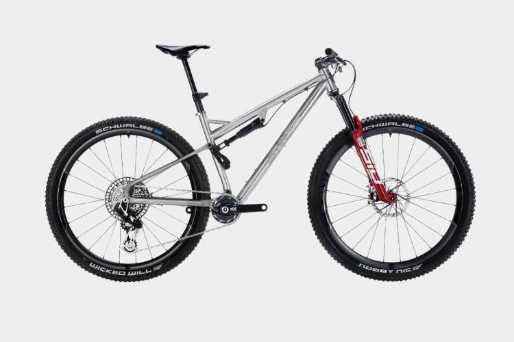 A silver mountain bike with a lightweight frame, featuring front suspension forks in red. It has black tires with labels "Schwalbe" and "Nobby Nic" on the sidewalls, and a modern gear setup with a rear cassette. The bike is positioned against a plain white background.