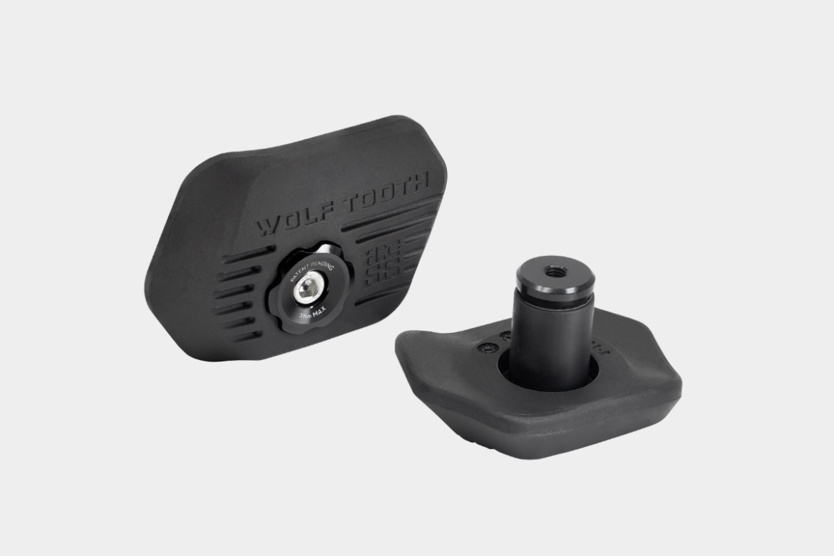 Image of a Wolf Tooth component featuring a black plastic base with a textured surface and a central adjustment knob. The knob is labeled with torque specifications, and another cylindrical black piece is positioned beside it. This component is likely part of a bicycle accessory designed for enhanced functionality or adjustments.