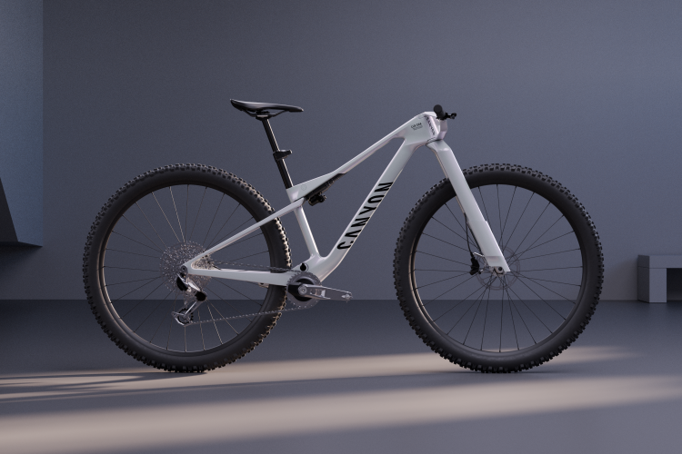A white mountain bike displayed in a minimalistic interior setting, featuring large, rugged tires and a sleek frame. The bike is positioned to show its geometric design and brand name, with soft lighting enhancing its contours against a subtle gray background.