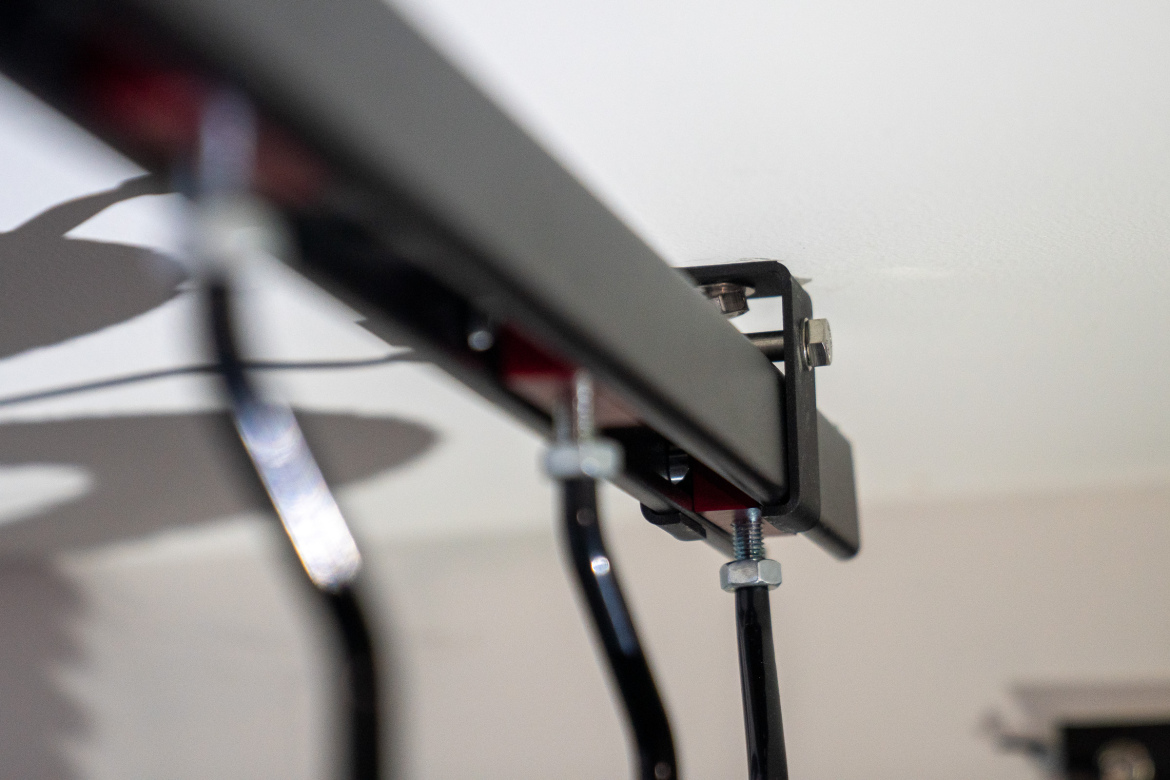 Close-up view of a ceiling-mounted track system, featuring metal components such as brackets, screws, and wires, against a light background.