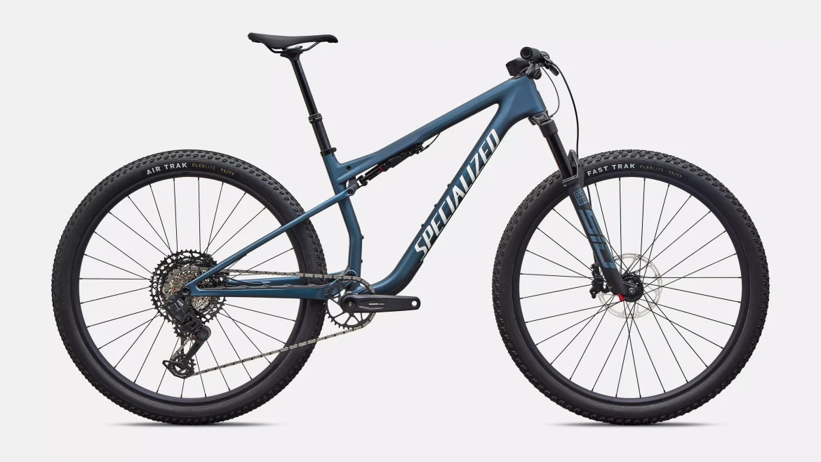 A blue mountain bike with a lightweight frame, featuring wide tires and a sleek design. The bike is equipped with disc brakes and a modern gear system. The background is plain, allowing the bike to be the focal point.
